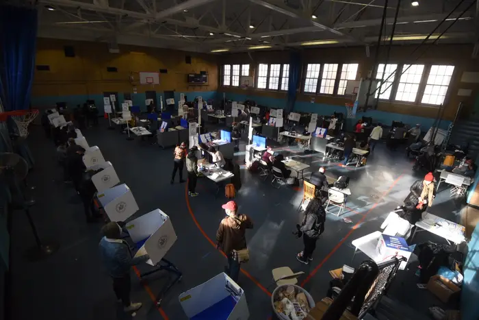 An aerial view inside the polling site at PS 192—voters are at privacy screens and scanners, with poll workers standing by scanners and sitting at the info desks.